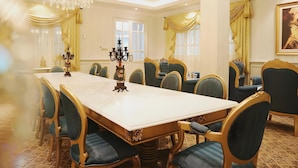 Une salle à manger élégante, avec une longue table, des chaises richement décorées et des lustres.