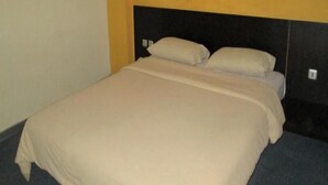 Un lit avec une tête de lit, une lampe fixée au mur et un mur sobre.