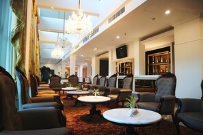 Vestíbulo de hotel con techo alto, candelabros, zonas de estar, un bar y una televisión.