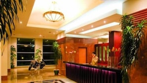 Un hall d’hôtel avec un comptoir d’accueil, une grande plante en pot et un lustre.