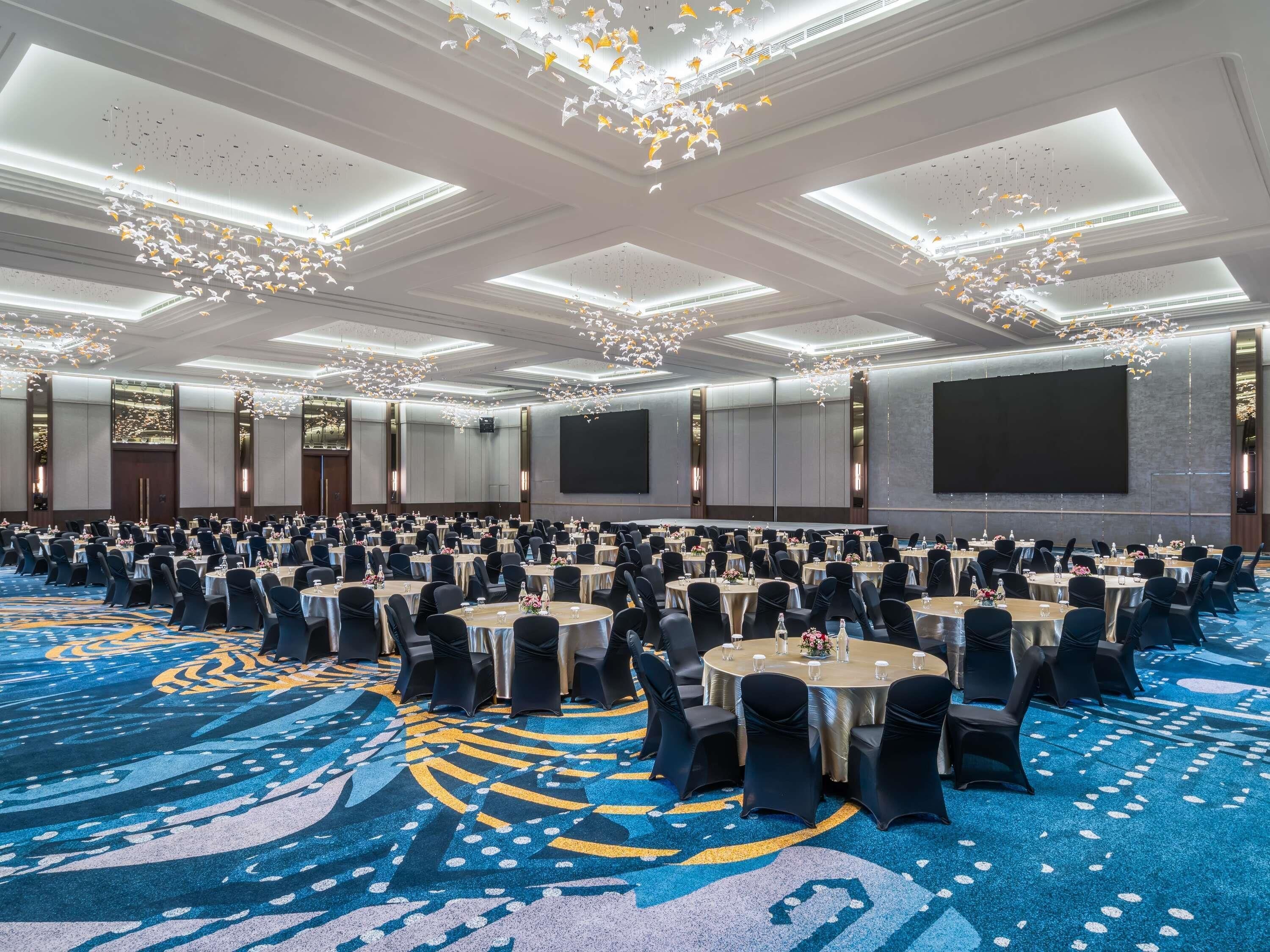 A large conference room with round tables, black chairs, and a blue carpet with a geometric pattern.