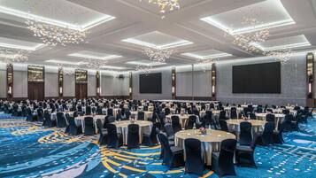A large conference room with round tables, black chairs, and a blue carpet with a geometric pattern.