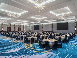 A large conference room with round tables, black chairs, and a blue carpet with a geometric pattern.