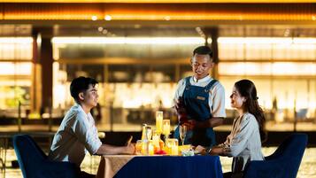 A dining table with a blue tablecloth, a waiter serving drinks, and a bar area in the background.