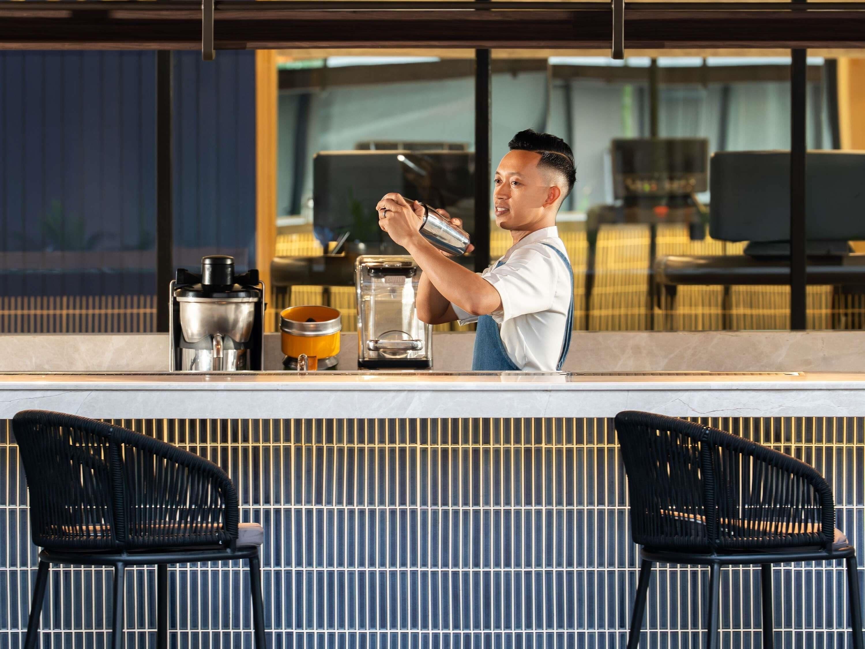 A bar area with a coffee machine, a glass container, and two chairs.