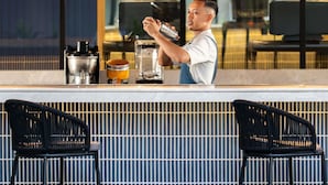 Una zona de bar con una cafetera, un recipiente de vidrio y dos sillas.