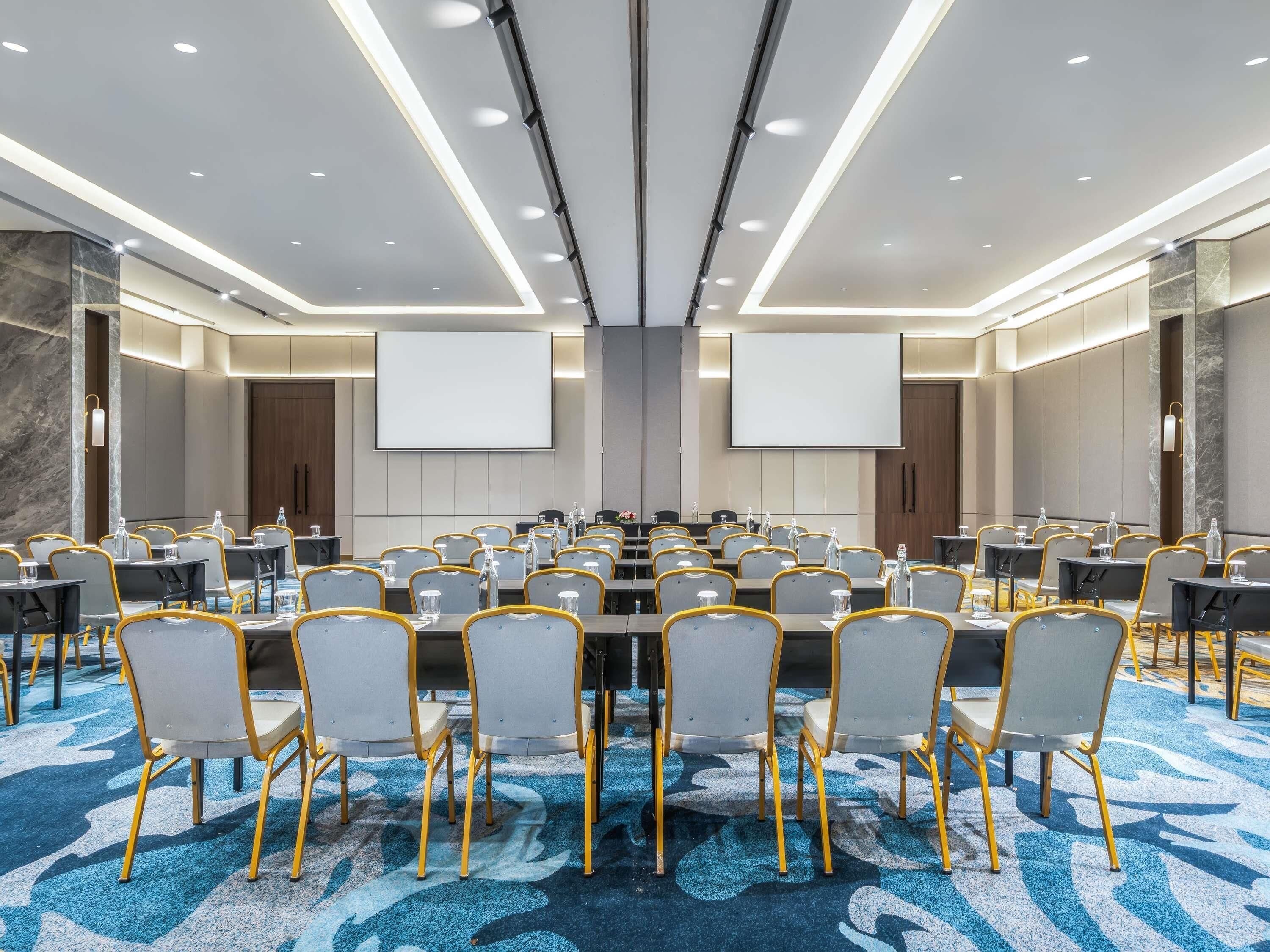A conference room with multiple tables and chairs, a large screen, and a carpeted floor.