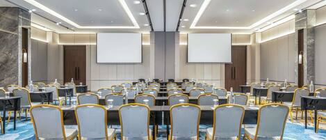 A conference room with multiple tables and chairs, a large screen, and a carpeted floor.