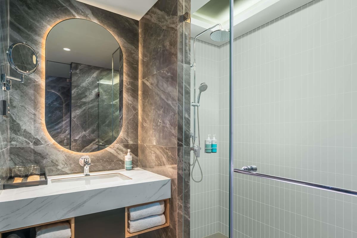 Une salle de bain moderne avec un meuble-lavabo en marbre, une douche à parois de verre et un miroir encastré.