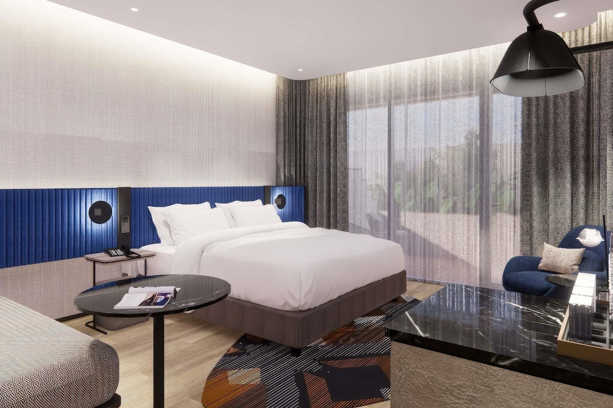 Une chambre d’hôtel moderne, dotée d’un grand lit, d’un bureau, d’une chaise et d’une grande fenêtre avec des rideaux.