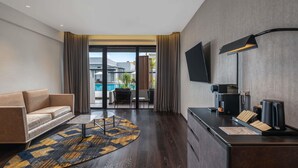 A modern hotel room with a sofa, a desk with a flat-screen TV, a coffee machine, and a view of a swimming pool. - Novotel Pontianak Convention Centre (Pontianak)