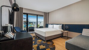 Moderni hotellihuone, jossa on suuri sänky, työpöytä, tuoli ja näkymä ulos.
