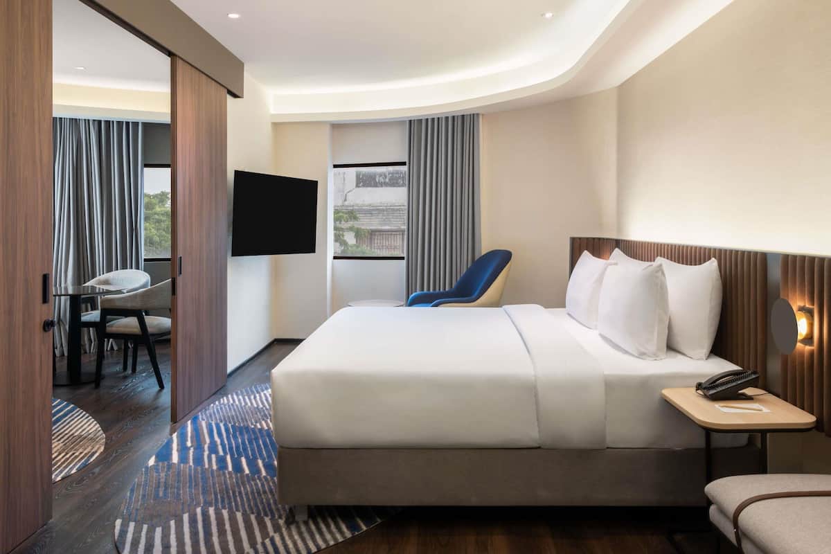 Een hotelkamer met een bed, een bureau, een stoel, een televisie en een raam met gordijnen.