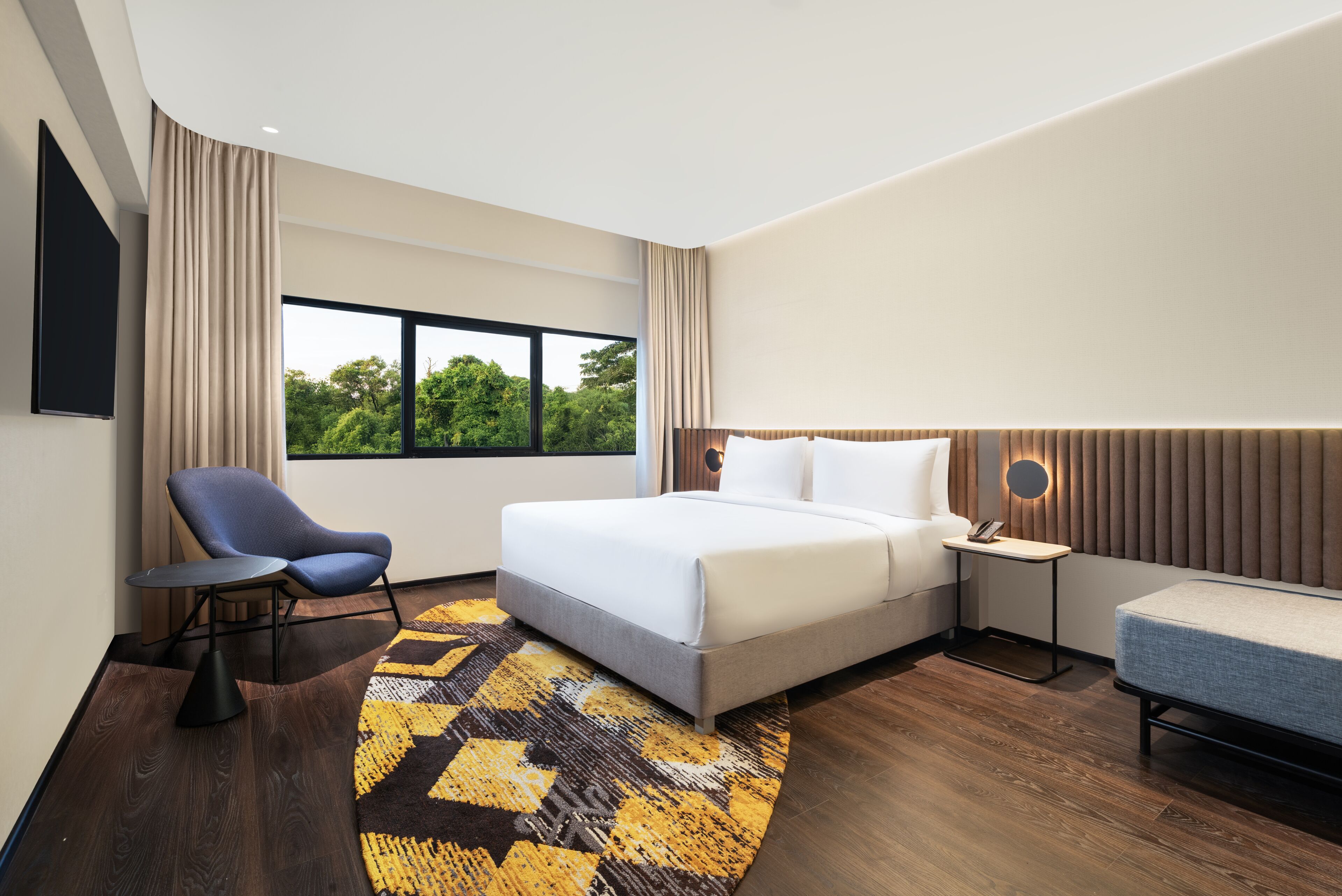 Una habitación de hotel moderna con una cama grande, un escritorio, una silla y vistas a zonas verdes.