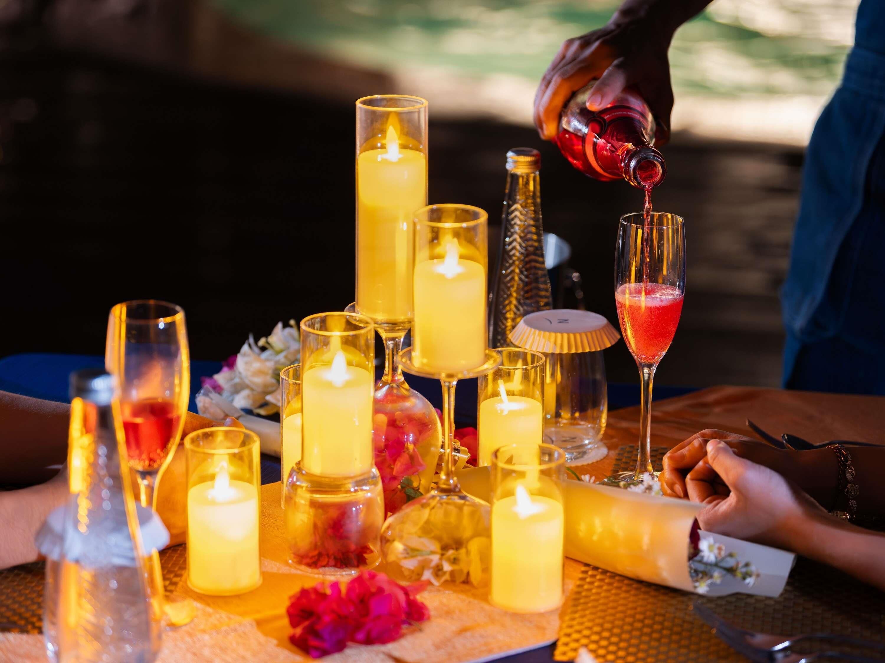 Une table avec des bougies, des verres et une bouteille dont on verse le contenu dans un verre.