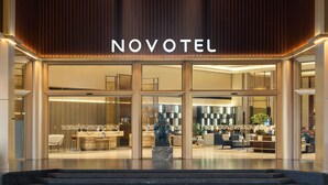 Exterior de un hotel de diseño moderno, con un llamativo letrero 'NOVOTEL', amplias ventanas de vidrio y una entrada bien iluminada.
