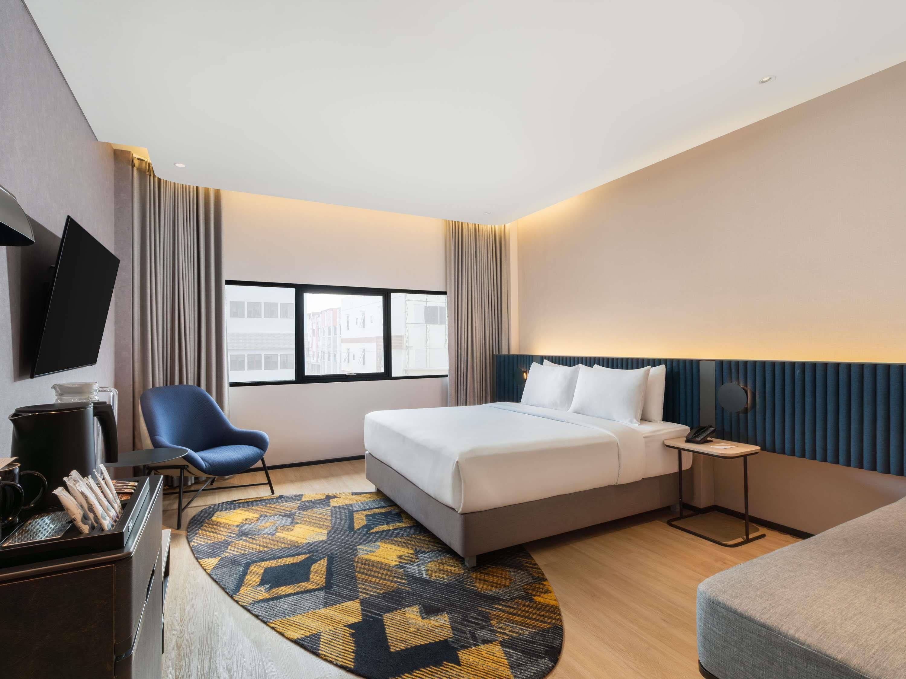 Une chambre d’hôtel équipée d’un lit, d’un bureau, d’une chaise, d’une télévision et d’une fenêtre donnant sur la ville.