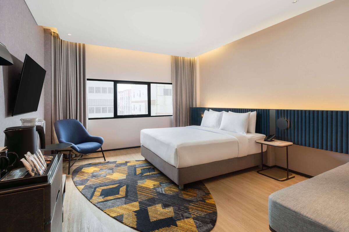 Une chambre d’hôtel équipée d’un lit, d’un bureau, d’une chaise, d’une télévision et d’une fenêtre donnant sur la ville.