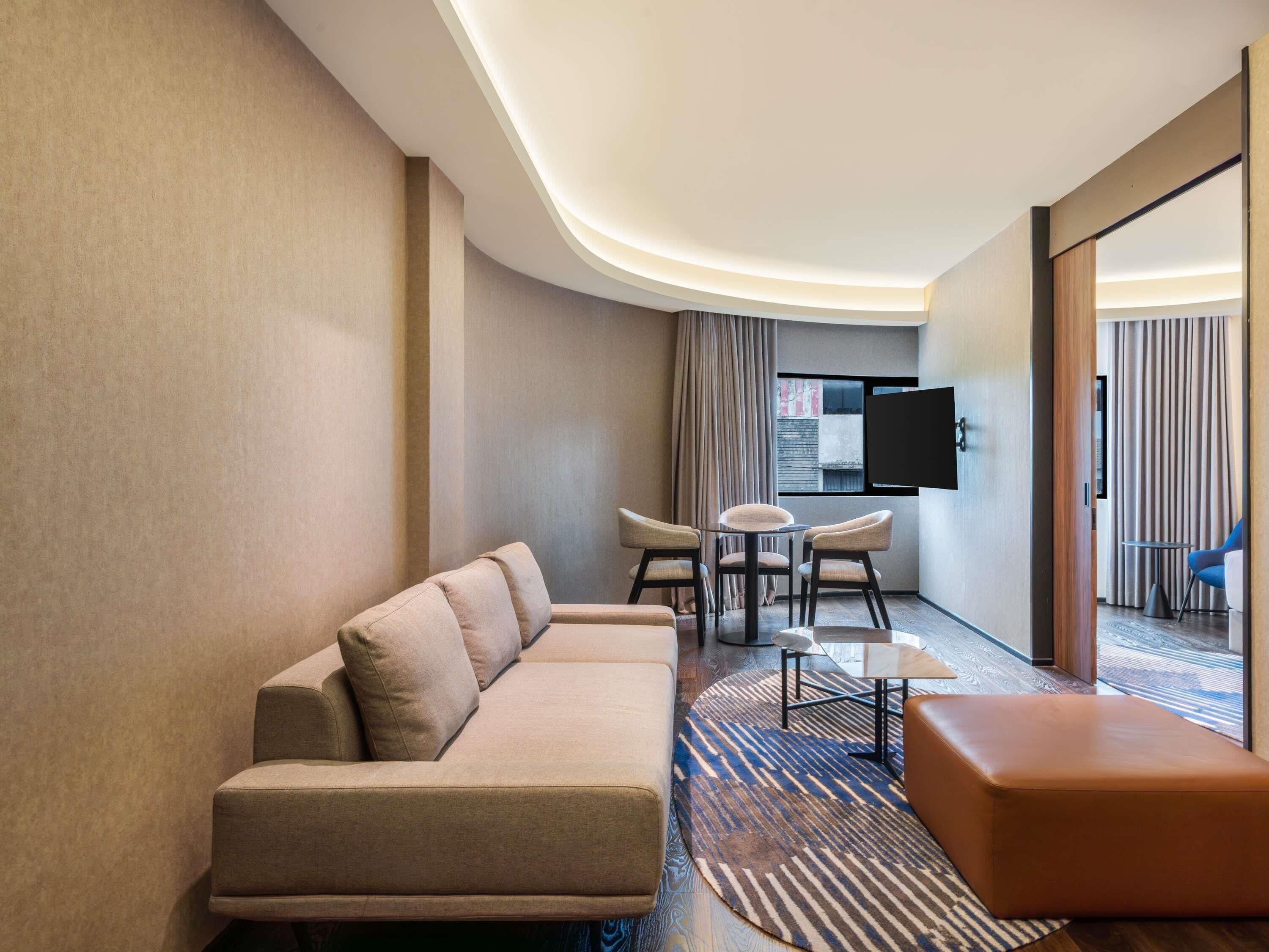 Une chambre d’hôtel moderne, équipée d’un canapé, d’une table basse, d’une télévision et offrant une vue sur l’extérieur.