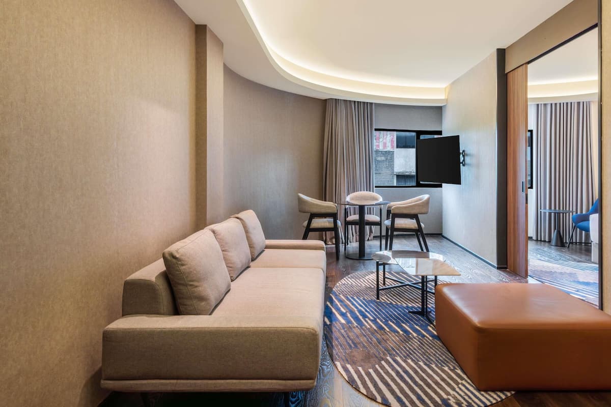 Une chambre d’hôtel moderne, équipée d’un canapé, d’une table basse, d’une télévision et offrant une vue sur l’extérieur.
