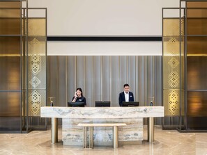 Ein Empfangsbereich mit zwei Mitarbeitern, einer Marmor-Theke und einem modernen Interieur mit vertikalen Paneelen und gemusterten Trennwänden.
