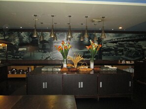 A bar area with a dark counter, multiple pendant lights, and a mural on the wall. - Kini Pontianak (Pontianak)