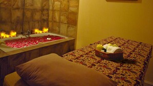 A bathroom with a bathtub filled with rose petals, candles, and a shower. There is a bed with a floral bedspread and a basket of toiletries. - Bumi Senyiur (Samarinda)