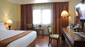 A hotel room with a large bed, a desk with a chair, a television, and a window with curtains. - Grand Victoria Samarinda (Samarinda)