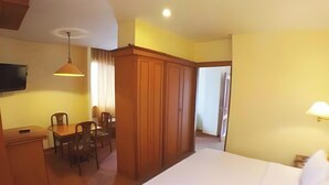 Una habitación de hotel con cama, escritorio, sillas, televisor y armario.