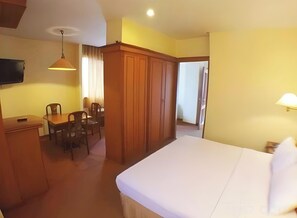 A hotel room with a bed, a desk, chairs, a television, and a wardrobe. - Amans (Ambon)