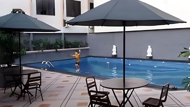 Una piscina techada con trampolín, rodeada de asientos y sombrillas al aire libre.