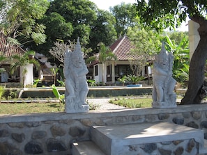 A courtyard with stone statues, a tiled-roof building, and lush greenery. - Bali Dream House (Karangasem)