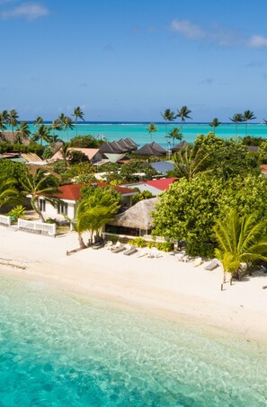 Un resort frente a la playa con cabañas de techo de paja, palmeras y aguas turquesas cristalinas.