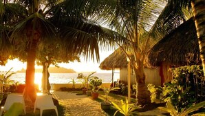 A beachside resort with thatched-roof huts, palm trees, and lounge chairs by the water. - Village Temanuata (Bora Bora)