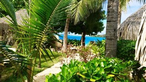 A tropical garden with palm trees, a thatched-roof structure, and a view of the ocean. - Village Temanuata (Bora Bora)