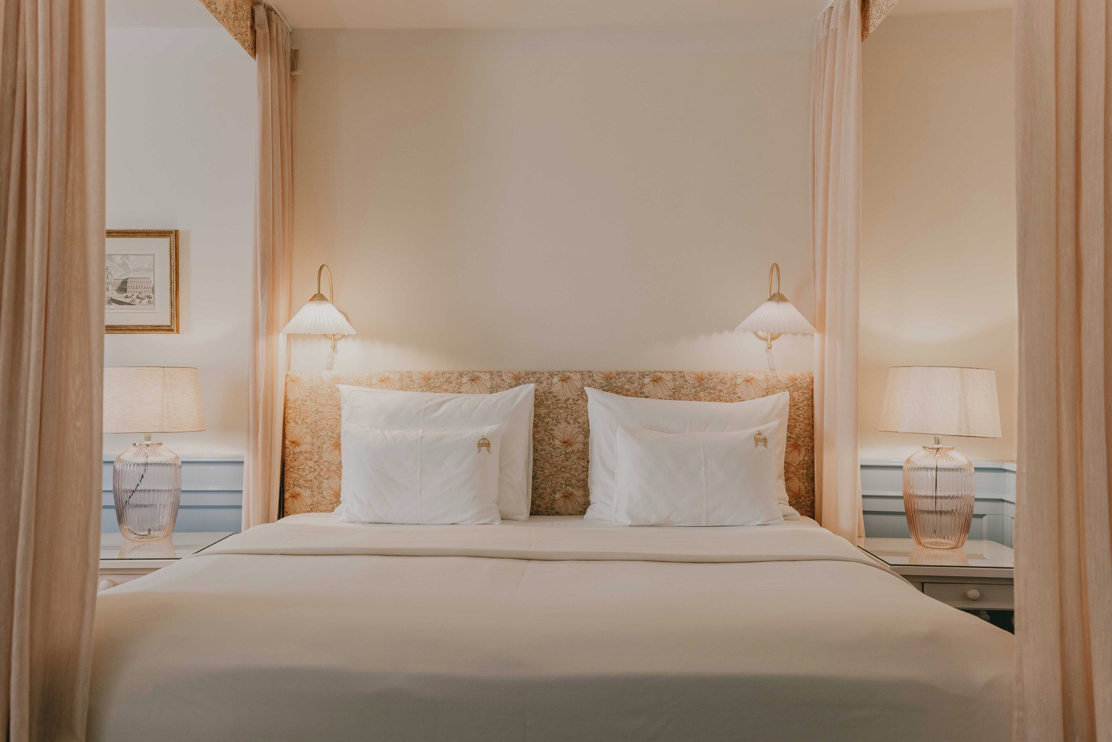 A hotel room with a large bed, two bedside lamps, and a floral-patterned headboard.