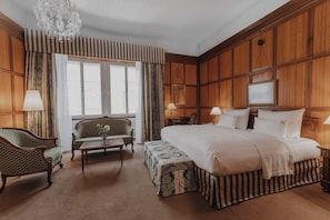 Habitación de hotel con una cama grande, un sofá, una mesa y una araña.