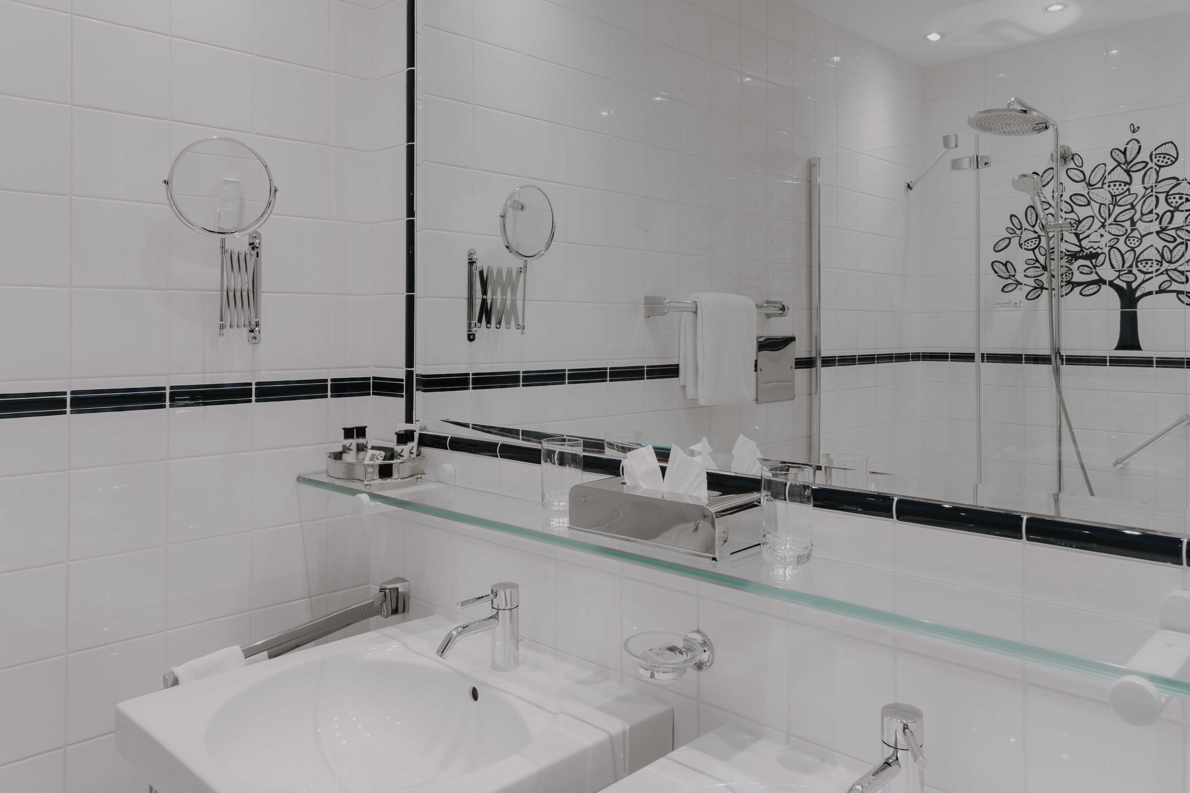 A modern bathroom with a glass shelf, two sinks, a mirror, and a shower with a tree decal.