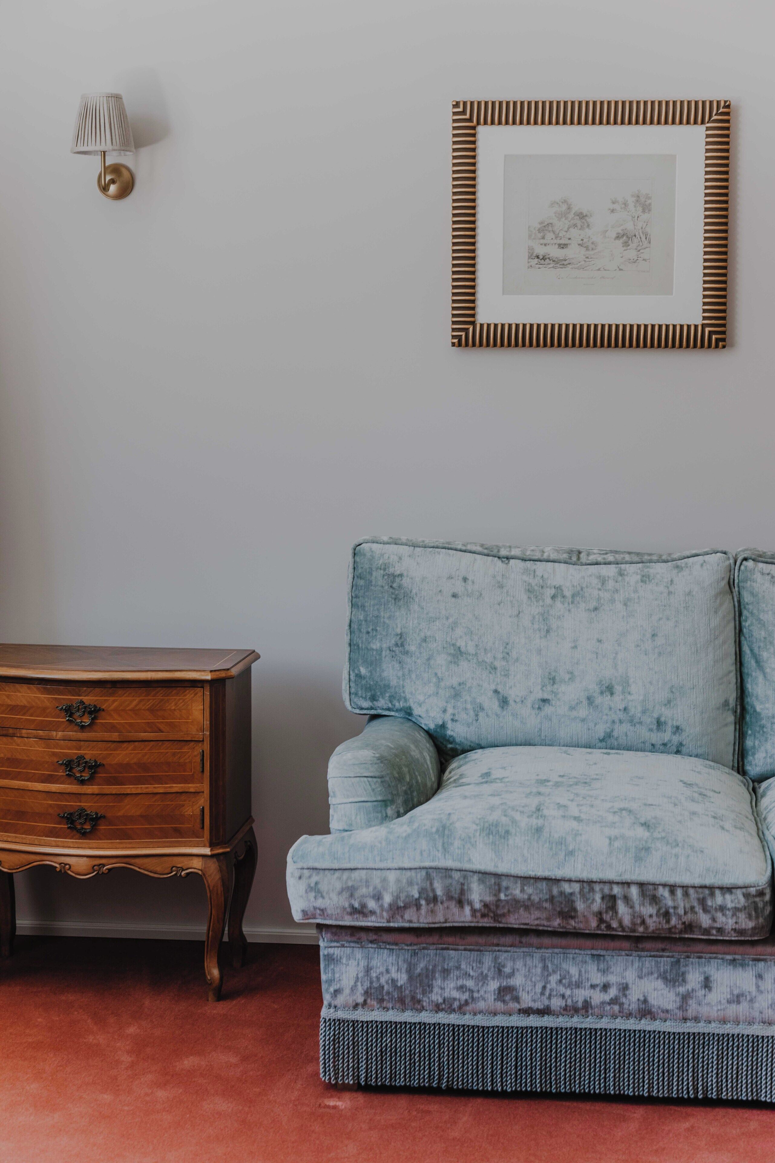 Una habitación con un sofá antiguo, un aparador de madera y un cuadro en la pared.