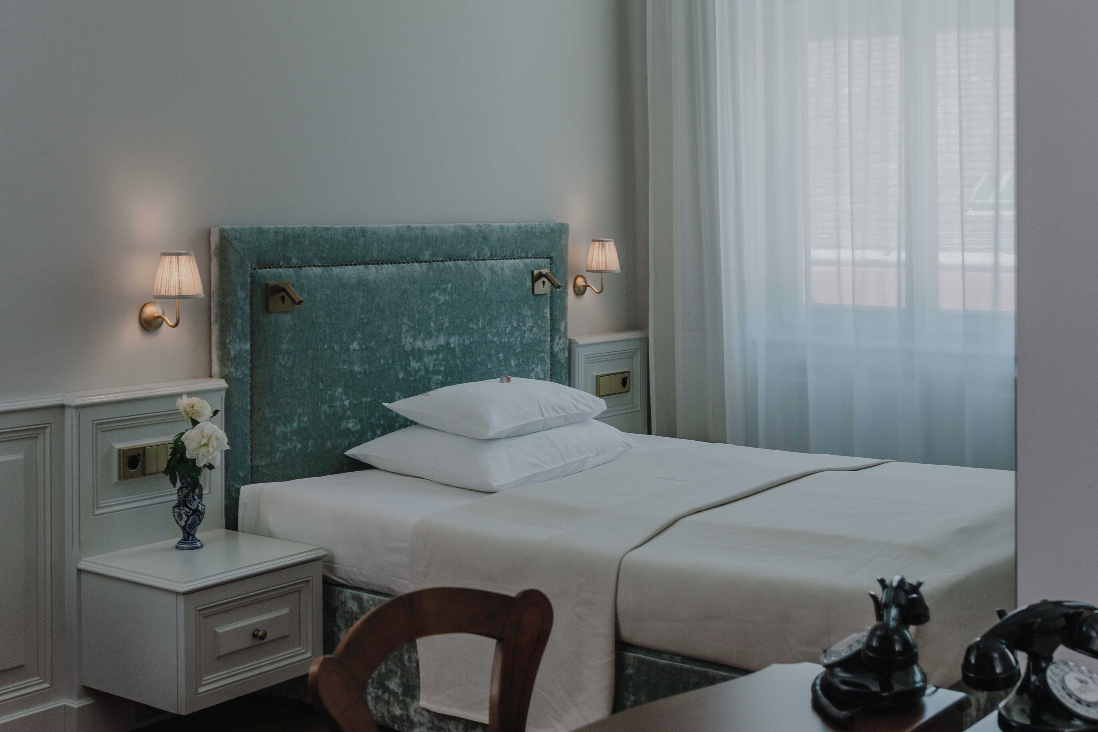 A neatly made bed with white linens, a teal headboard, and two bedside lamps.