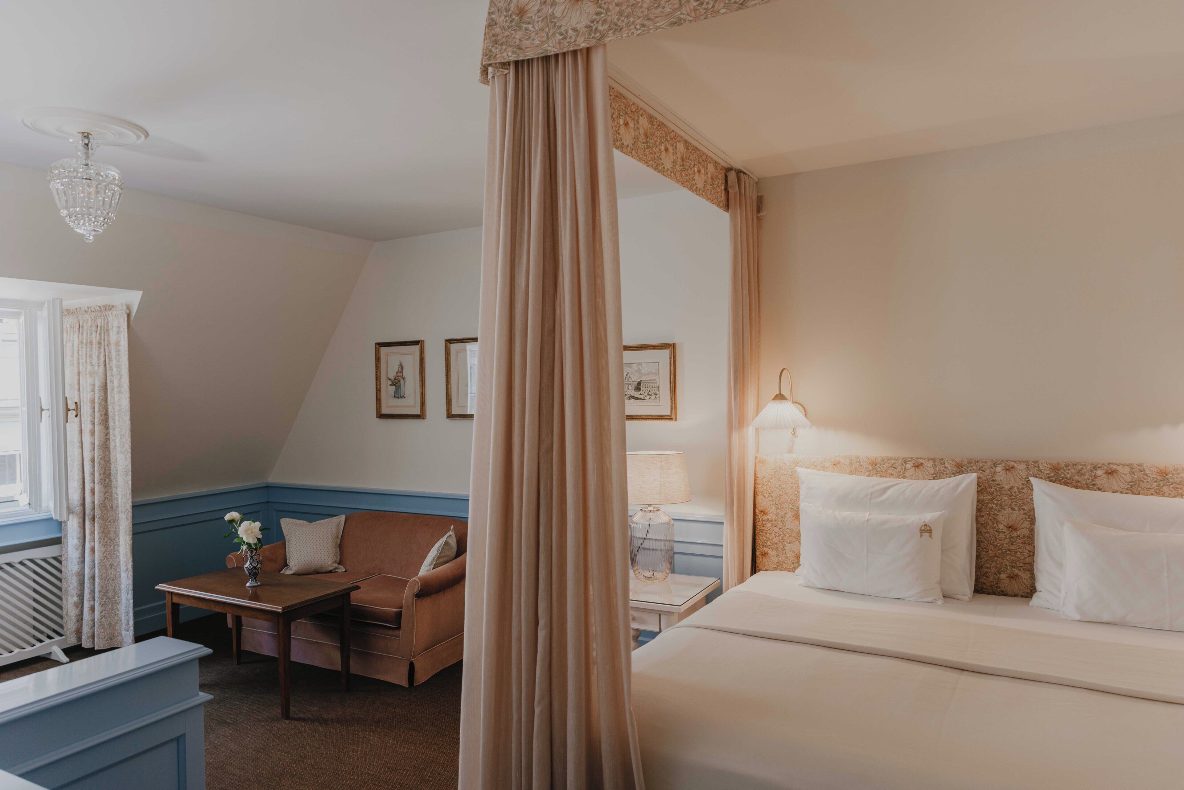 A hotel room with a bed, a chair, a desk, a lamp, and a window with curtains.