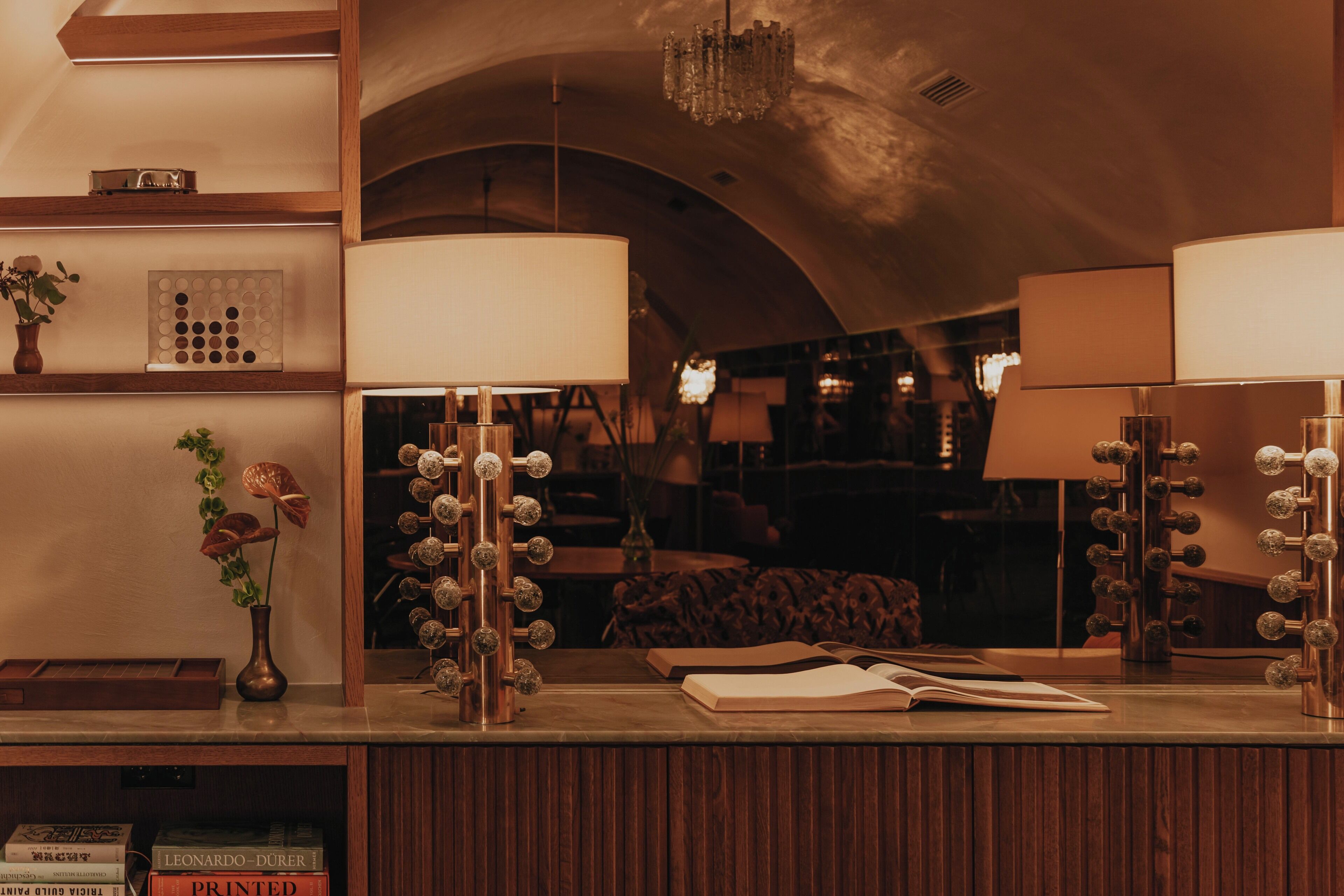 Un salón bien iluminado con un mostrador de recepción de madera, un candelabro y un espejo grande con luces.