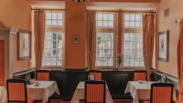 A dining room with four tables, each with a white tablecloth and orange chairs.