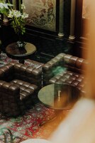 A room with a patterned carpet, a round glass table, and a sofa with a cushioned backrest.