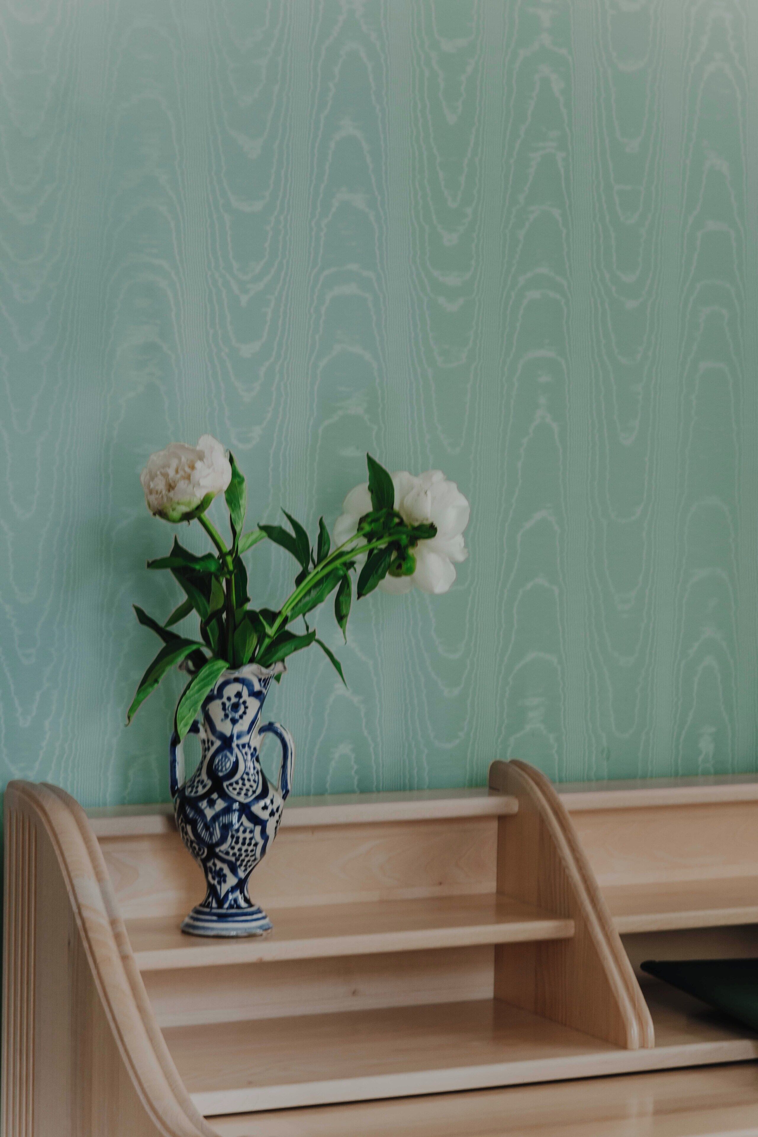 Een houten plank met een blauwe en witte vaas gevuld met witte bloemen.