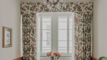 A room with a green sofa, a round wooden table, a chandelier, and floral curtains.