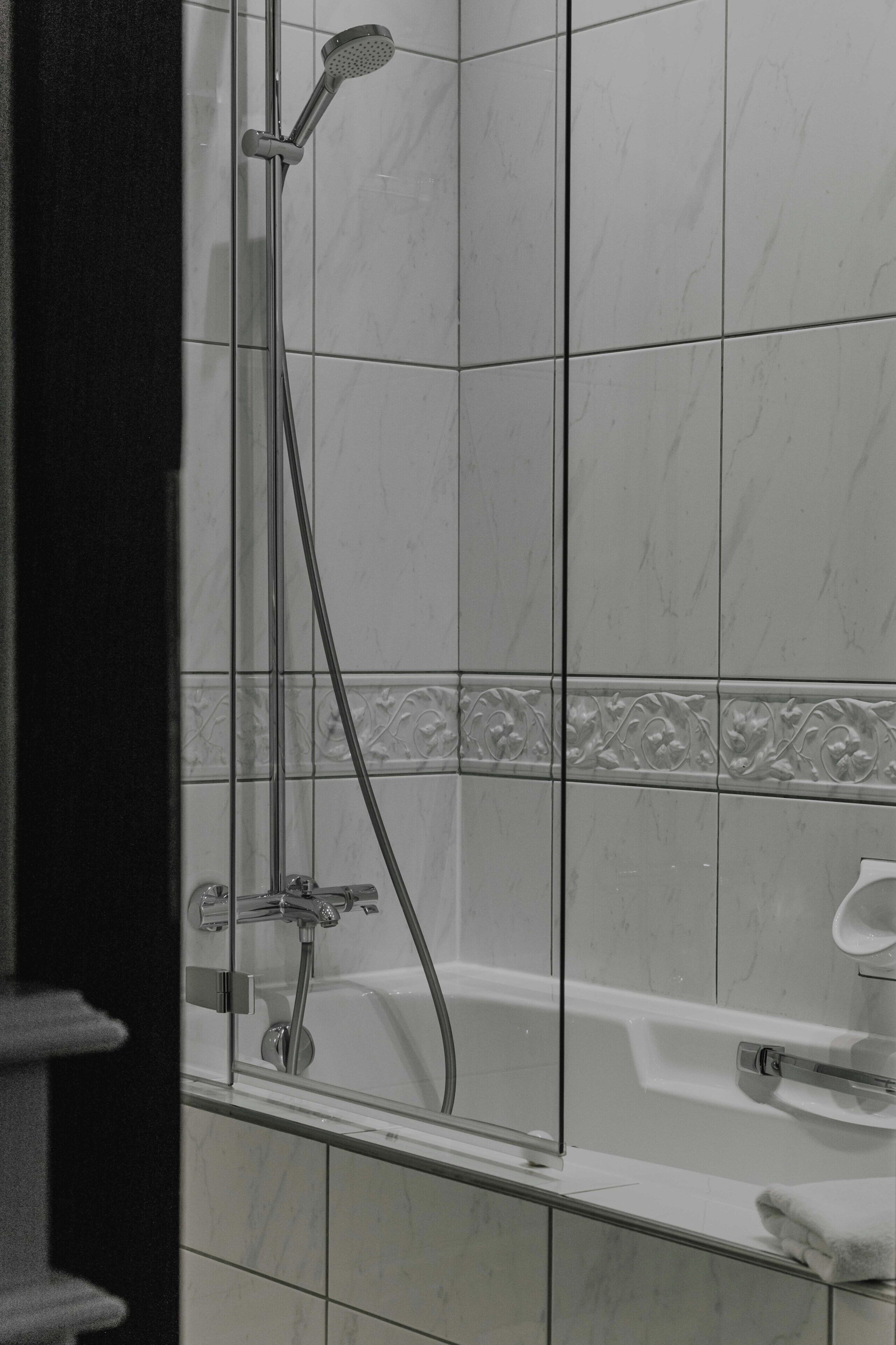 A shower area with a glass door, a handheld showerhead, and a bathtub with a faucet.