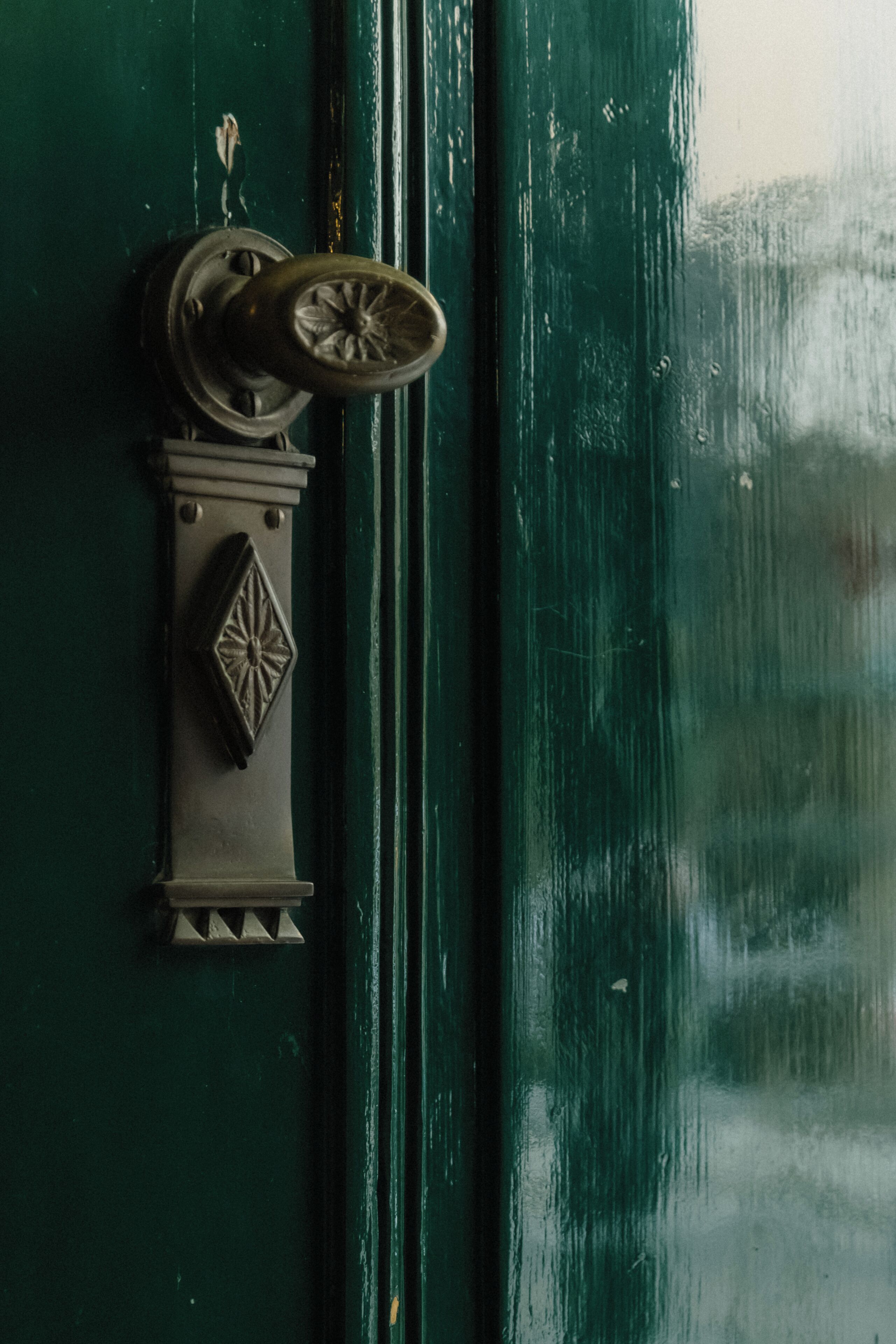 Una puerta verde con un picaporte de latón y una placa decorativa.