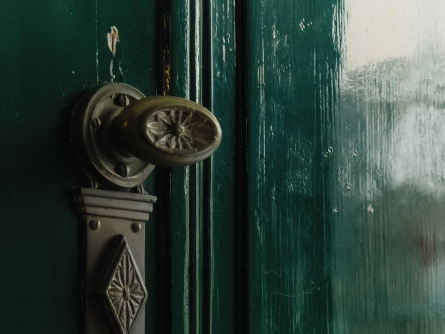 Una puerta verde con un picaporte de latón y una placa decorativa.
