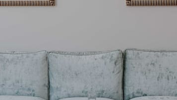 Una sala de estar con un sofá, una mesa de centro de vidrio y dos obras de arte enmarcadas en la pared.